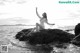 A woman sitting on a rock by the ocean.