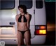 A woman in a black bikini standing in front of a van.