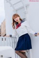 A woman in a sailor outfit leaning against a wall.