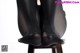A woman sitting on top of a wooden chair wearing black stockings.
