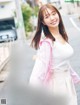 A woman in a white shirt and pink jacket standing on a street.